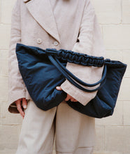 Load image into Gallery viewer, Pazar Tote XL Navy plant dyed nylon mood picture I French lady is wearing the bag casually with one hand under her arms leaning against a wall in Paris I Zoomed in picture with focus on the bag.