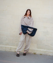 Load image into Gallery viewer, Pazar Tote XL Navy plant dyed nylon mood picture I French Lady is wearing the bag casually with one hand under her arms leaning against a wall in Paris.